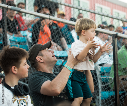 A father and his two sons sitting in the stadium stands, cheering and supporting their favorite team. A happy family enjoying a sports event together, showing excitement, teamwork, and the spirit 