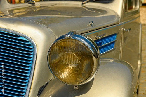 Close-up of a vintage car's shiny metallic silver exterior and blue grille. Detailed view of the front fender, headlight, and iconic grille of a classic automobile, showcasing its retro design and
