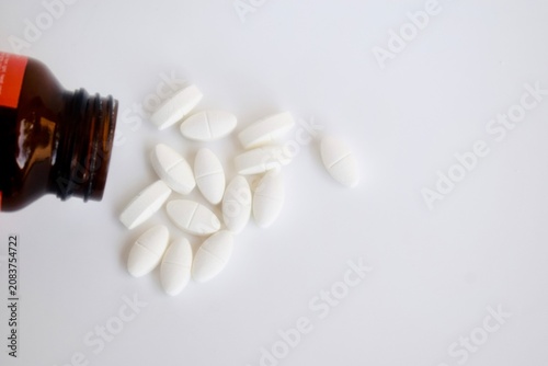 Принти на полотні Top down view of white oblong prescription medicine caplets scattered on a white surface next to an open amber glass bottle