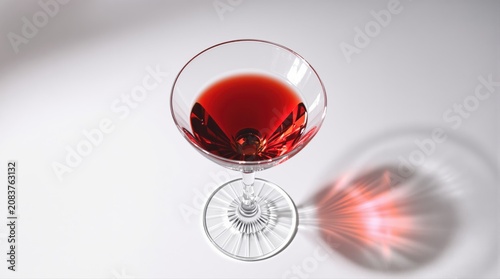 A coupe glass filled with a ruby-red drink casts a dramatic shadow.