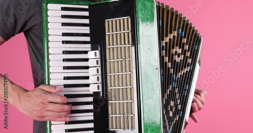 Man playing piano accordion on pink background, closeup