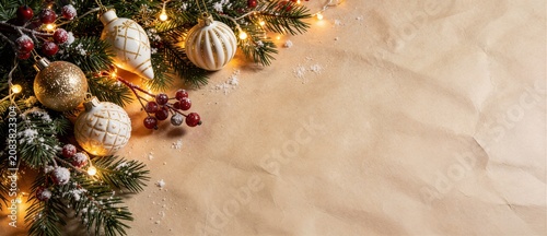 Charming Christmas fir branches with white ornaments and red berries on crumpled craft paper ideal for rustic holiday website banner