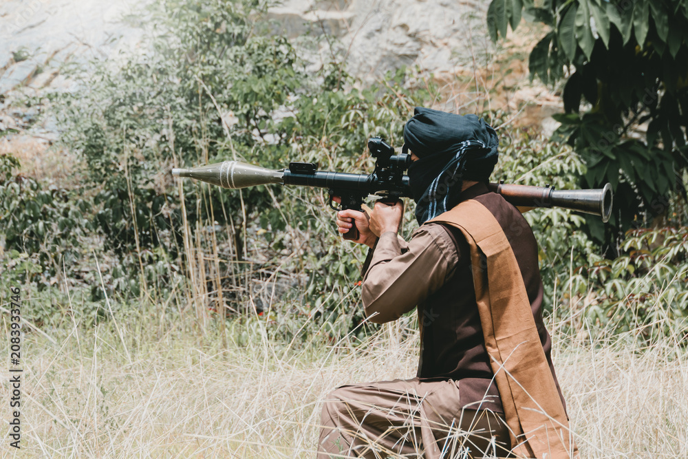 Fototapeta premium Outdoor military concept. Armed man, kneeling soldier in grass with rocket launcher in outdoor field