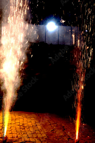 Ground Firework Fountains – Twin Orange Yellow Sparks with Glowing Trails, Smoke and Brick Surface Against Dark Festive Night Concept