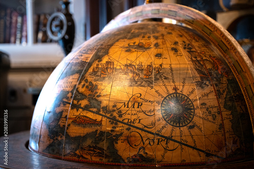 Obraz na plátne Close-up of an antique decorative globe featuring an old world map with books and study decor softly blurred in the background