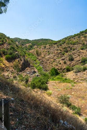 A rugged river gorge winds through parched scrubland and rocky terrain in the hills of Portugal. Dense green shrubs follow the seasonal watercourse as eucalyptus and oak trees crown the dry hillsides