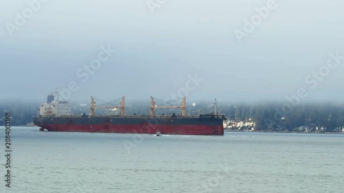 Bulk carrier cargo ship anchored in misty bay near coastline, Vancouver