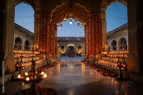 Traditional Indian wedding decor with oil lamps and marigolds, festive palace courtyard at dusk, luxury event entrance with floral drapes and diya lighting
