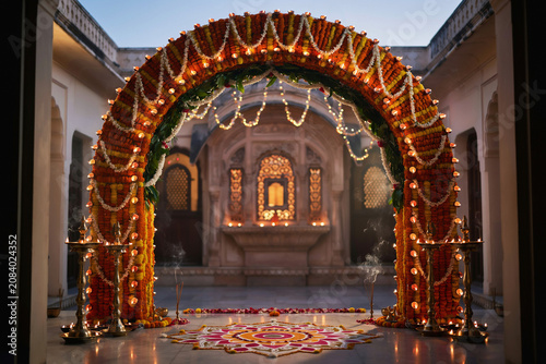 Traditional Indian wedding arch with marigold flowers, ornate floral entrance for Hindu marriage ceremony, luxury palace courtyard decoration with oil lamps