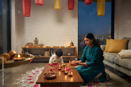 Diwali celebration at home with Indian mother and child, traditional oil lamps and rangoli on floor, festive Hindu holiday decorations