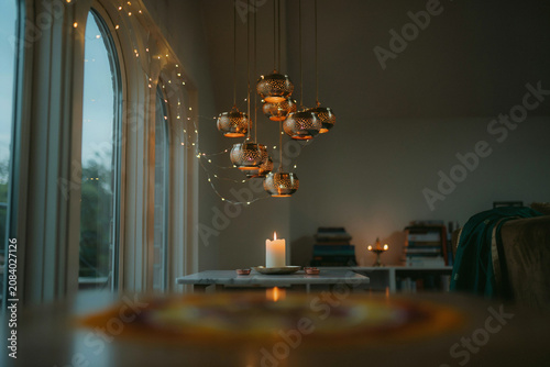 Atmospheric interior with hanging golden lanterns, warm candle light on a table, cozy home sanctuary with fairy lights and arched windows