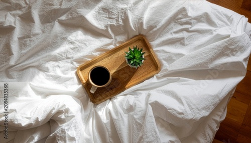 A serene wooden tray holding a hot cup of morning coffee and a small decorative succulent plant rests peacefully on crisp white wrinkled bedding