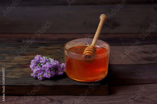 Fresh organic honey in a glass bowl with a wooden dipper, surrounded by fragrant purple thyme blossoms on a rustic wooden surface