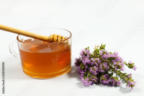 Golden thyme honey in a glass cup, featuring a wooden dipper and a bunch of fresh thyme flowers, representing natural sweetness and wellness