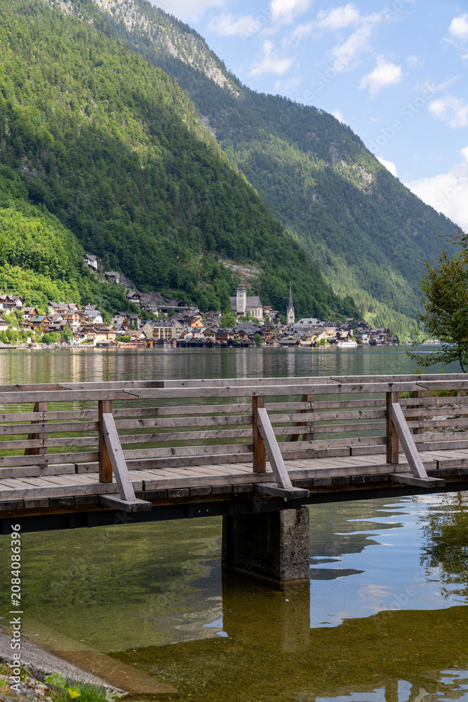 Fototapeta premium Wooden footbridge with traditional alpine village and mountains in the background