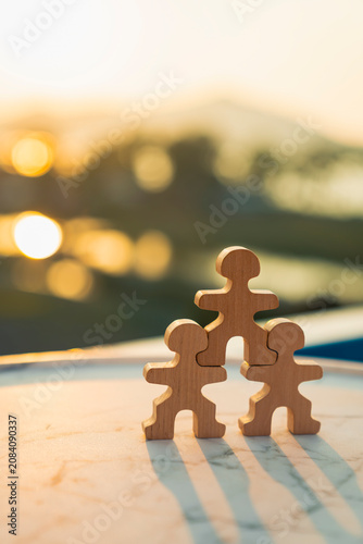 Wooden human figures puzzle stacked in pyramid with sunset background, representing teamwork cooperation, business leadership, support unity, and strong family foundation.