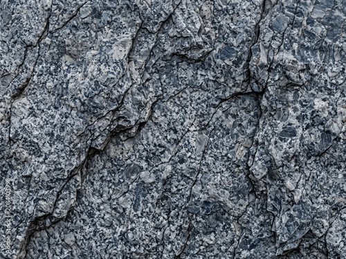 Rough grey rock surface with deep cracks and granular texture.