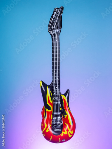 Close-up of a blow-up toy shaped like a guitar on a purple background, highlighting its bright colors and playful design