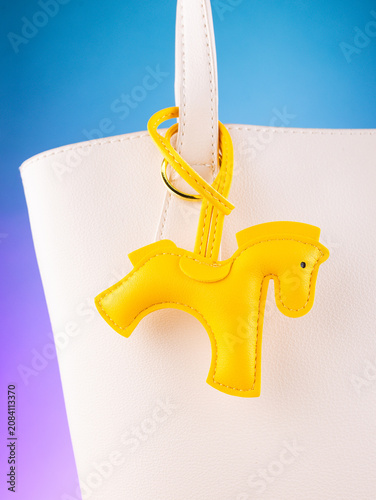 Fotografie Close-up of a leather bag charm with a yellow horse, placed on a white  bag