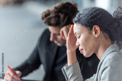 Stressed young businesswoman holding head working project about problem on laptop and documents during intense office discussion in business meeting with colleague workplace deadline pressure.