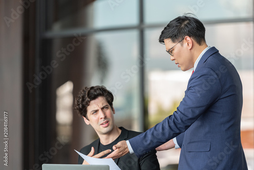 Фотография Stressed young businessman holding head in hand receiving criticism by manager after discussing document error on laptop for work mistake at outdoor office business pressure leadership feedback