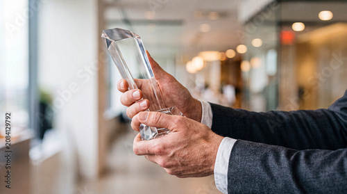 Fotografie Close-up photograph of a businessman in a suit holding a clear, multifaceted glass award trophy