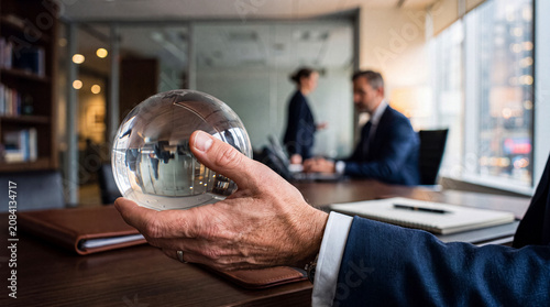 Photos Confident businessman's hand holding a clear glass globe in a bustling office, symbolizing global reach and leadership