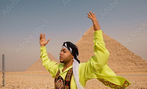Φωτογραφία Egyptian man in vibrant neon embroidered robe lifts both arms skyward with eyes