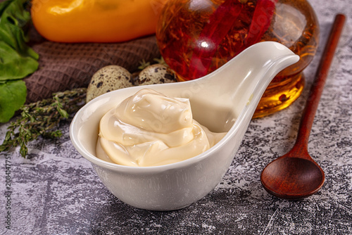 Fotografie Creamy mayonnaise in white ceramic bowl with quail eggs and herbs on textured su