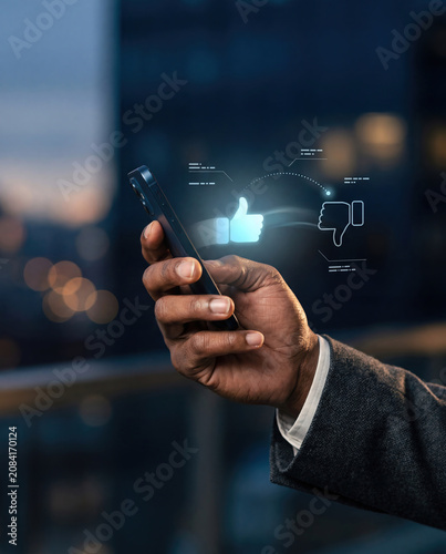 Unrecognizable businessman holding a smartphone with holographic thumbs up and thumbs down icons, AI content review and human approval concept at dusk
