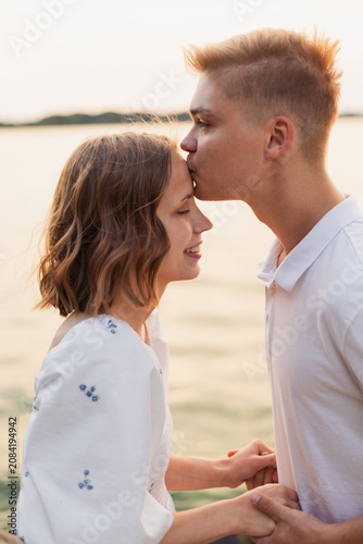 Canvas Print Young couple shares a tender moment with a forehead kiss at sunset by the water