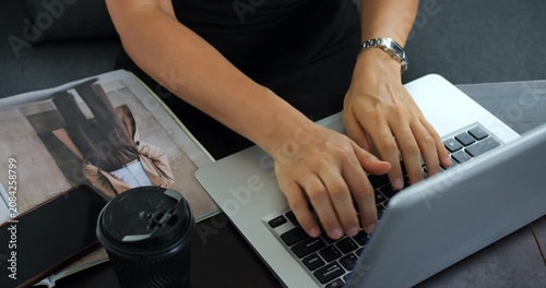 Hands typing on laptop keyboard in closeup, writer composing email and document next to coffee and magazine steady focused motion conveys deadlinedriven content creation in small home office.
