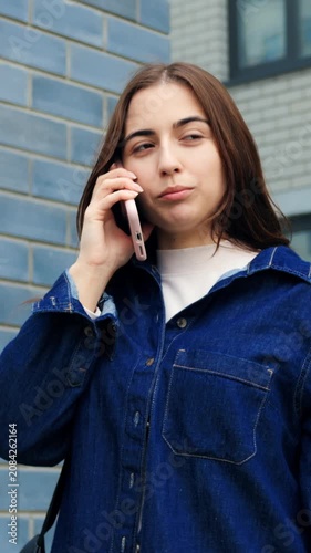 Urban woman waiting. Woman in denim overlooking city entrance. Caucasian lady with backpack standing by brick wall. Individual in casual attire glancing at watch beside urban building facade