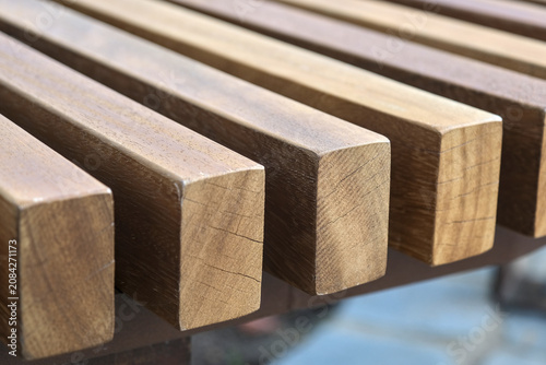Schilderij op canvas Modern wooden bench with clean slatted design and metal frame on a stone pavement, showcasing natural texture and minimalist outdoor style