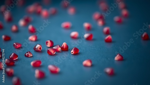 Close-up of pink pomegranate seeds scattered on a dark blue surface with detailed texture.