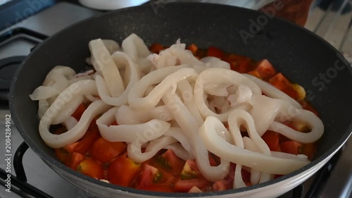 Seafood cooking close-up of calamari rings gently placed over sizzling cherry tomato slices in a pan, perfect for Mediterranean recipe, food blog, and culinary content