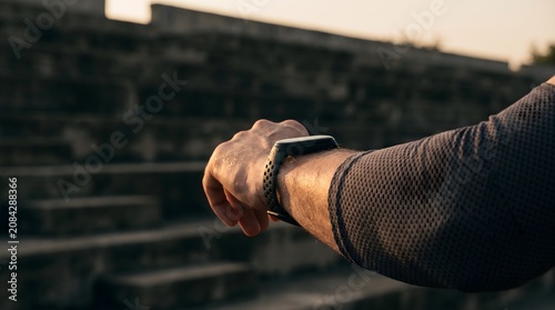 Close up of athlete arm checking smartwatch fitness tracker during outdoor workout at sunset