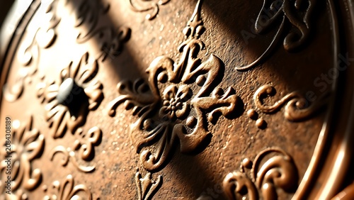 Raised ornamental patterns on a copper plate with strong side lighting.