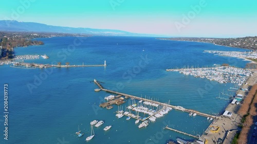 Aerial view of Geneva harbor on Lake Geneva, Switzerland, with jetties, lighthouse, moored sailboats and marinas along Quai Gustave-Ador on a clear winter day, Jura mountains on the horizon.
