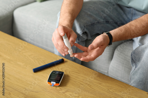 Foto Diabetic young man using lancet pen on sofa at home, closeup