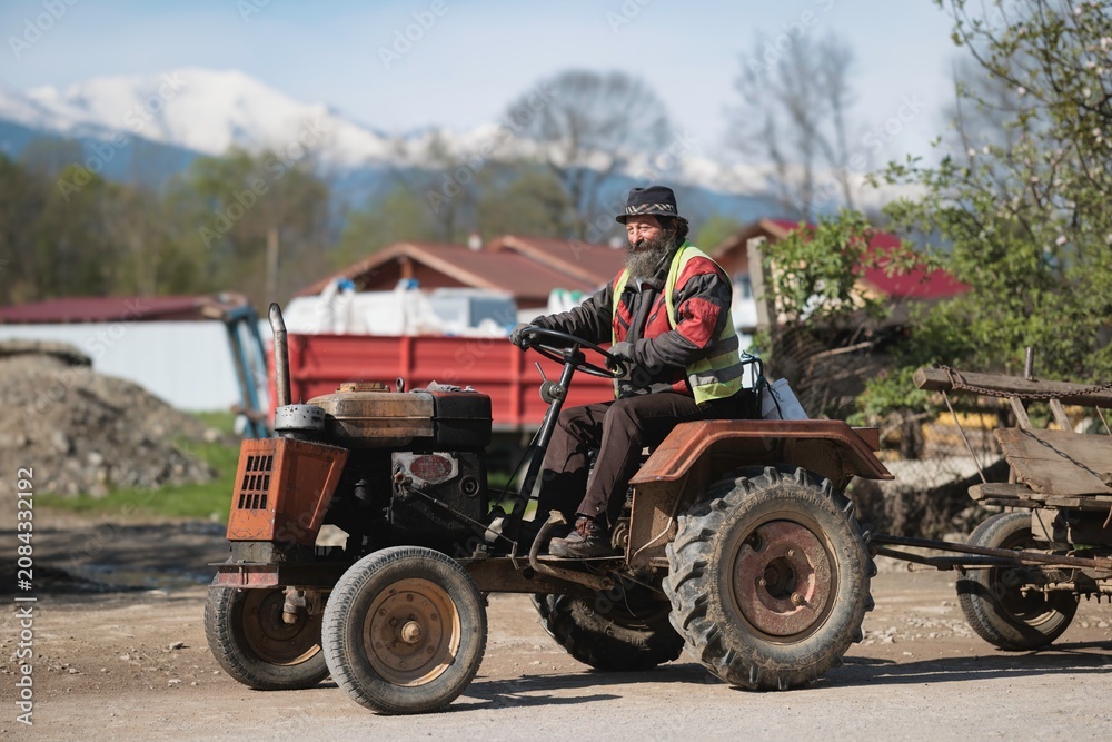 Fototapeta premium A seasoned farmer drives a classic tractor through a quaint countryside, showcasing traditional farming techniques