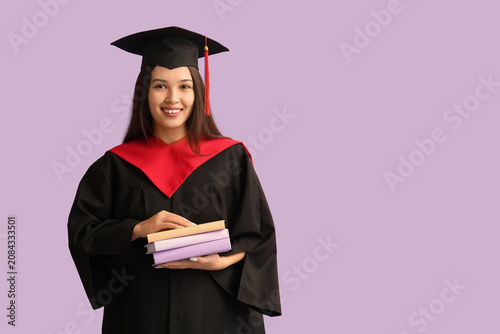 Young female graduate with books on lilac background
