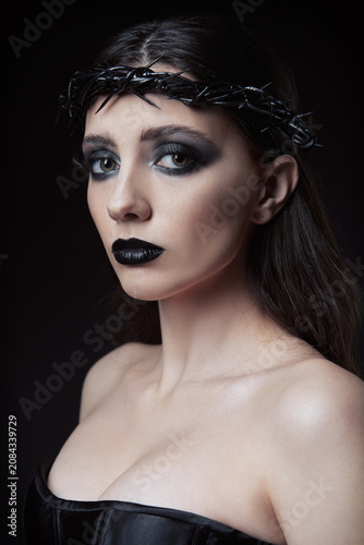 Close-up studio portrait of the gorgeous goth girl. Lovely informal (gothic) lady with black crown of thorns on head