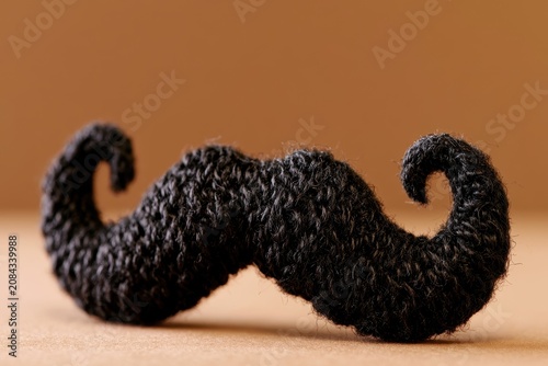 handmade black knitted mustache crafted from soft wool yarn sitting on  warm brown surface