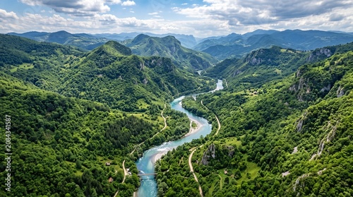 Quadro su tela Aerial view of a winding alpine river flowing through a lush green valley surrou