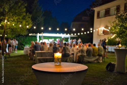 Cozy outdoor summer garden party at night with candlelight and blurred people background.