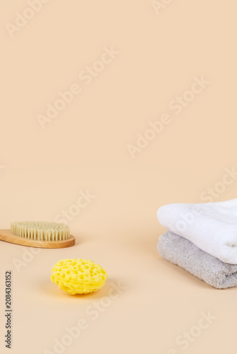 Minimalist spa and beauty product mockup background with copy space. Wooden body brush, yellow sea sponge, and stacked towels on warm beige background for cosmetic presentation.