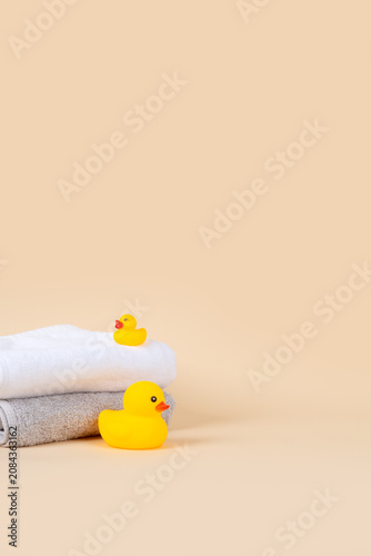 Baby bath product mockup background with vertical copy space. Cute yellow rubber ducks and stacked soft towels on warm beige background for newborn skincare presentation.