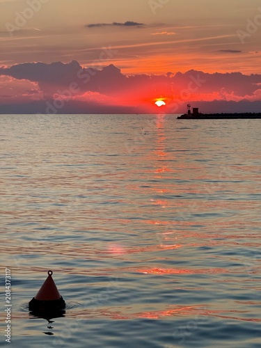 sunset in Trieste, Italy. The sun is setting behind the mountains but lights reflect on the Mediterranean Sea 