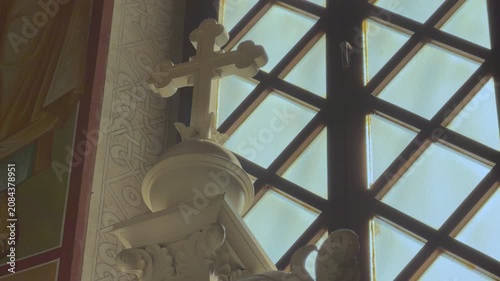 An ornate white sculpted cross and decorative carving inside an Orthodox church glowing softly beside a latticed bright window